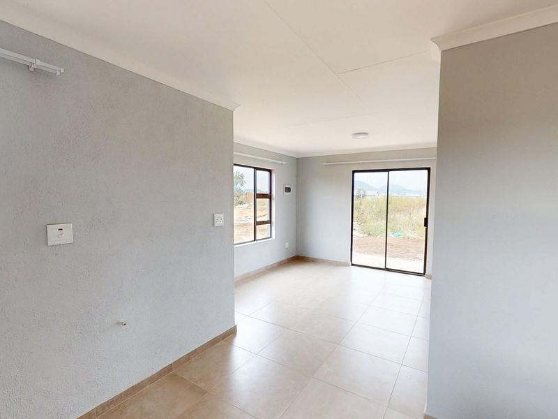 A bright, open-plan living area featuring neutral tiled flooring, modern aluminium window frames, and a sliding glass door leading to the exterior.