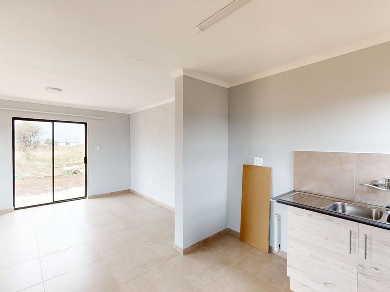 An open-plan living and kitchen area featuring tiled flooring, a compact kitchenette with a stainless steel sink, and a sliding door to the exterior.
