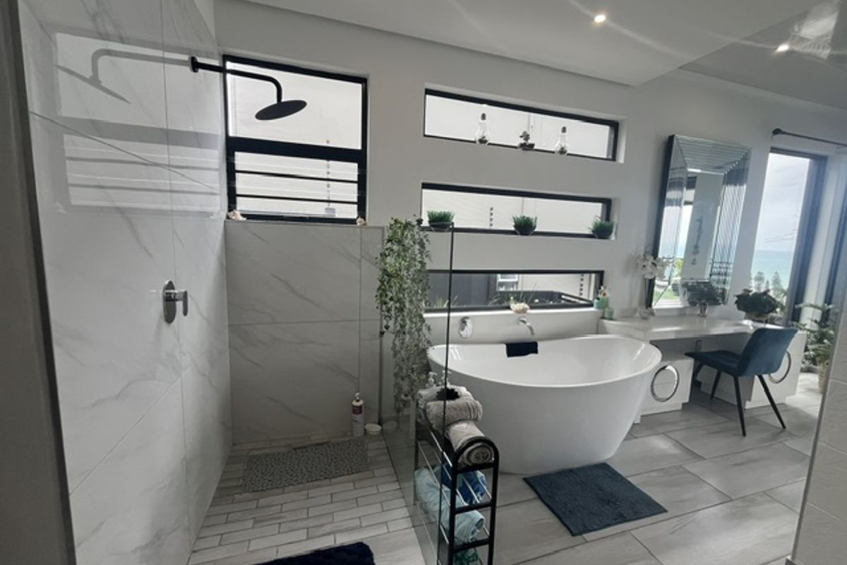 Modern bathroom featuring a sleek freestanding bathtub, a spacious walk-in shower with marble-look tiling, and a built-in vanity area.
