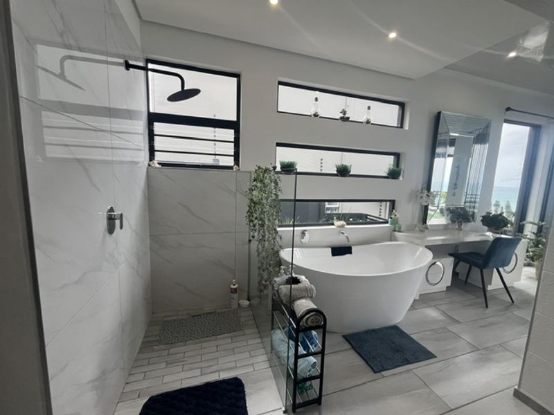 Modern bathroom featuring a sleek freestanding bathtub, a spacious walk-in shower with marble-look tiling, and a built-in vanity area.
