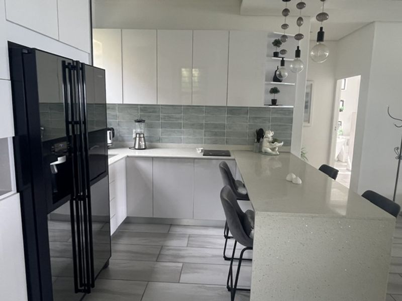 Modern kitchen featuring sleek white cabinetry, stone countertops, a subway tile backsplash, and a breakfast bar with pendant lighting.