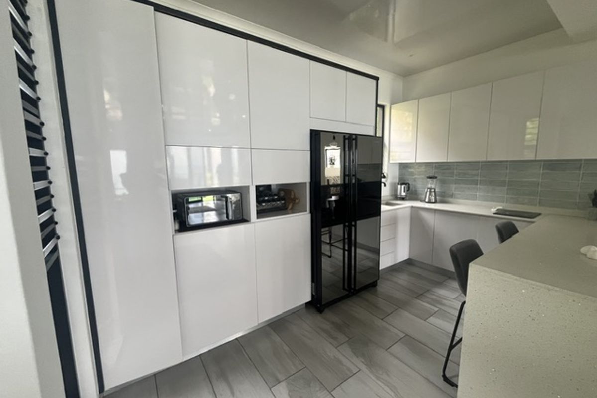 Modern kitchen featuring high-gloss white cabinetry, stone countertops, a tiled backsplash, and large format floor tiles with integrated appliance housing.