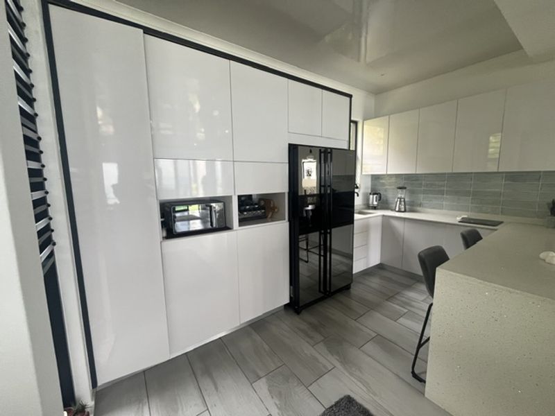 Modern kitchen featuring high-gloss white cabinetry, stone countertops, a tiled backsplash, and large format floor tiles with integrated appliance housing.