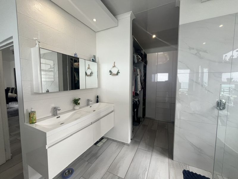 Modern bathroom featuring a sleek double vanity, wall-mounted mirror cabinet, and an integrated walk-in closet with high-end finishes and contemporary tiling.