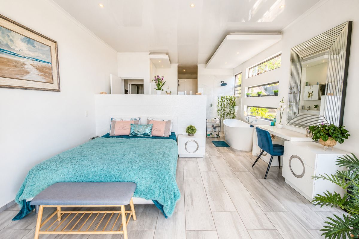 Spacious bedroom featuring an open-plan layout with an integrated freestanding bathtub, shower area, and built-in vanity with modern tiled flooring.