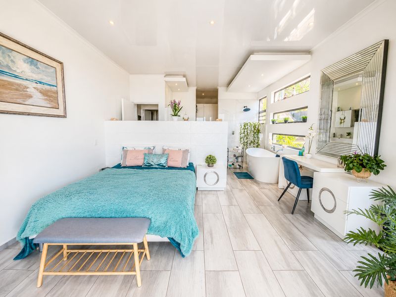 Spacious bedroom featuring an open-plan layout with an integrated freestanding bathtub, shower area, and built-in vanity with modern tiled flooring.