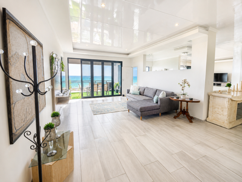 Spacious open-plan living area featuring glossy ceilings, recessed lighting, tiled floors, and large sliding doors opening to a scenic ocean view.