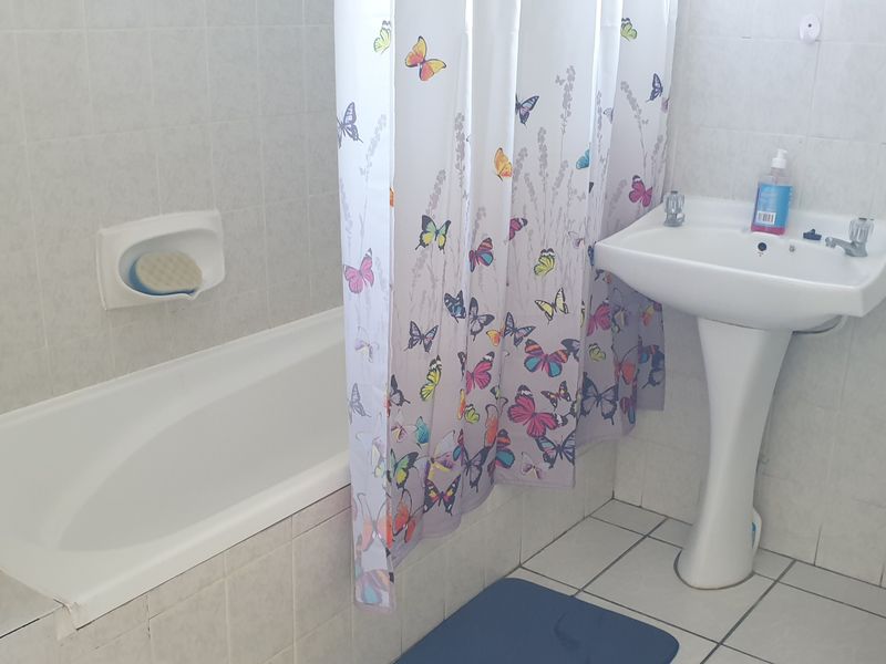 A functional bathroom featuring a pedestal basin, a built-in bathtub with shower attachment, and tiled finishes throughout.