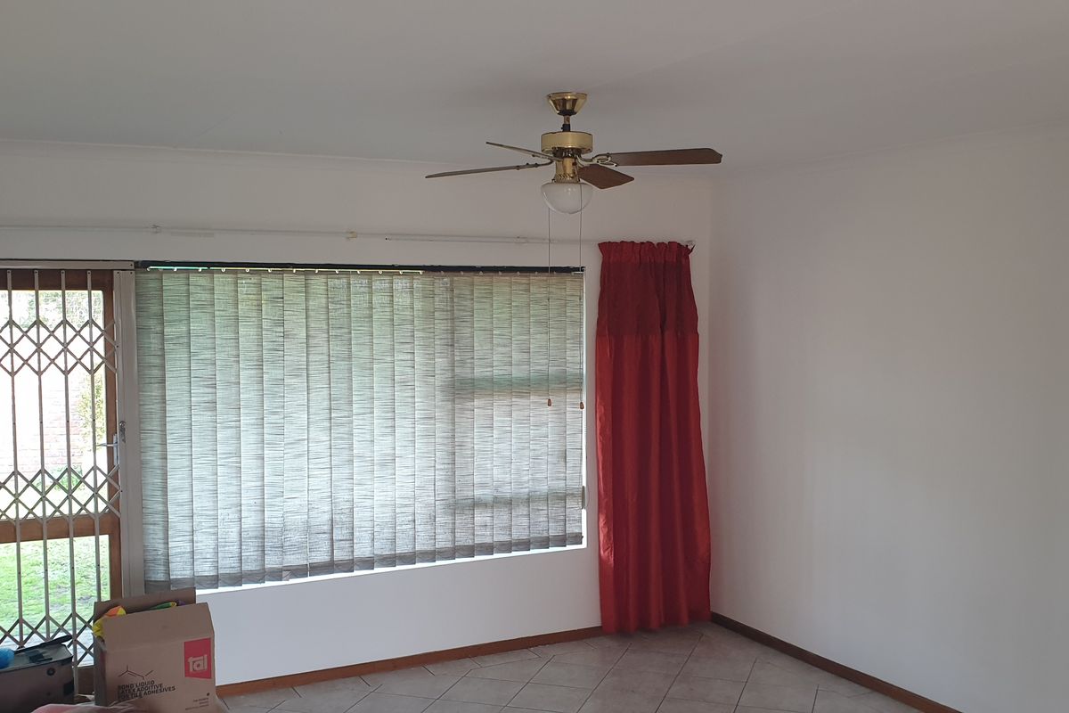 A bright, empty living room featuring tiled flooring, a ceiling fan, and a security gate leading to the exterior.