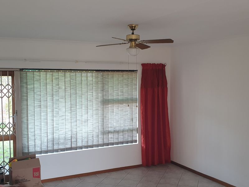 A bright, empty living room featuring tiled flooring, a ceiling fan, and a security gate leading to the exterior.