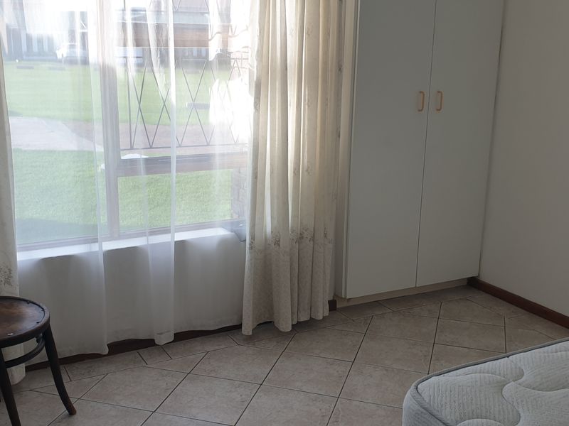 A simple bedroom featuring tiled flooring and a built-in wardrobe, offering a clean and functional space with natural light.
