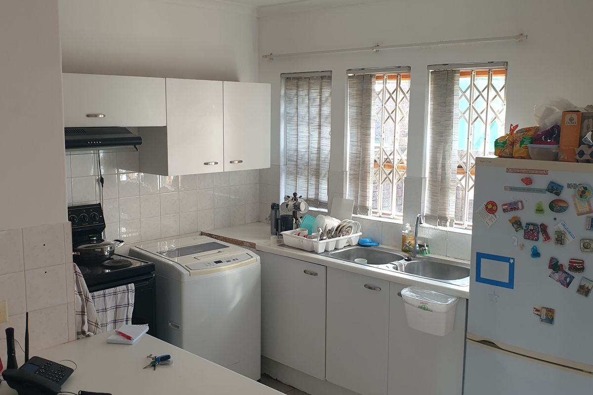 A functional kitchen featuring white cabinetry, tiled backsplash, double sink, and integrated extractor fan, with security bars installed on the windows.