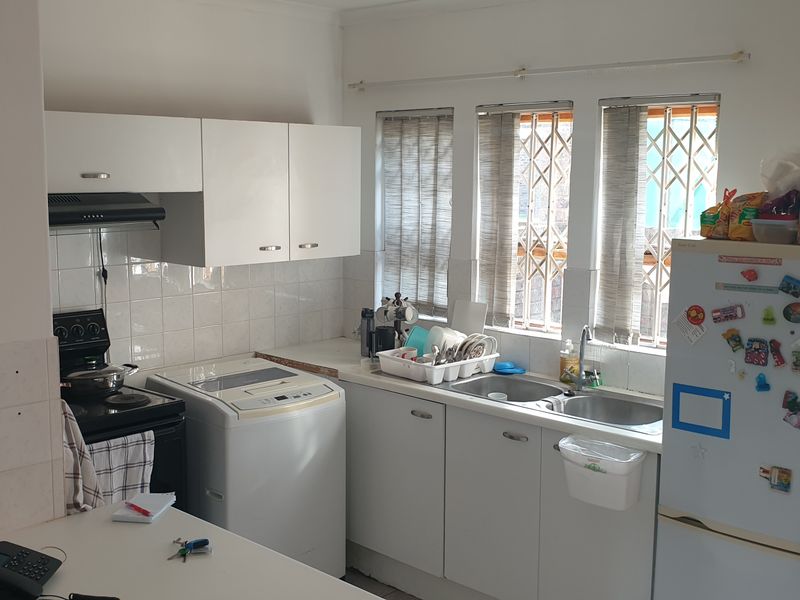 A functional kitchen featuring white cabinetry, tiled backsplash, double sink, and integrated extractor fan, with security bars installed on the windows.