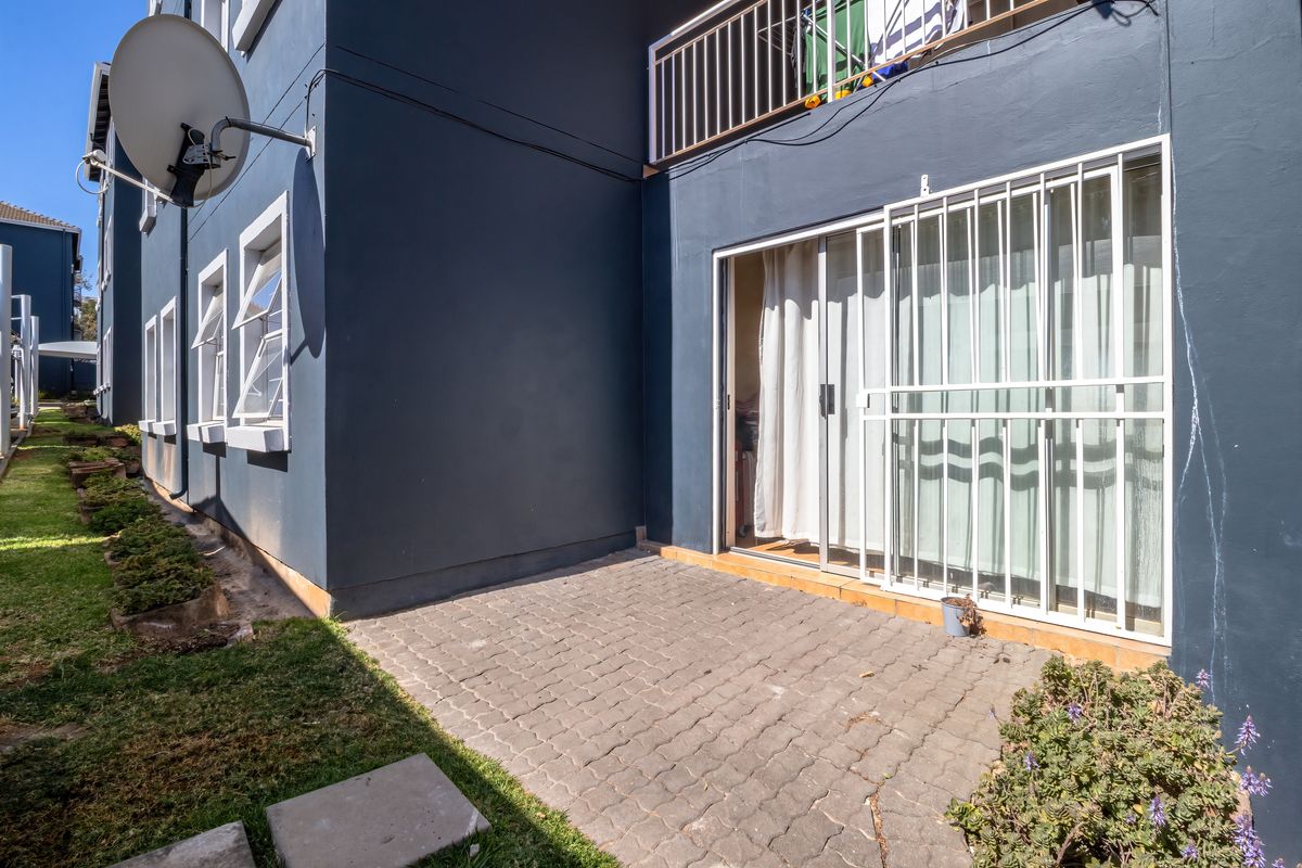 Rear exterior view of the apartment featuring a paved patio, sliding glass door with security gate, and balcony access above.