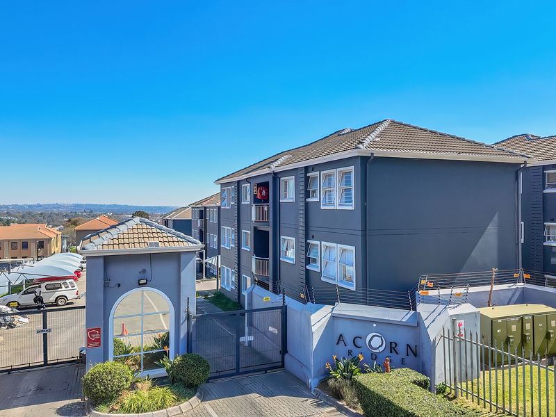 Exterior view of the Acorn Ridge apartment complex entrance, featuring a secure gated access point, paved driveway, and perimeter security fencing.