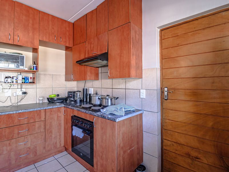 Compact kitchen featuring wooden cabinetry, built-in oven with extractor fan, tiled backsplash, and durable tiled flooring.