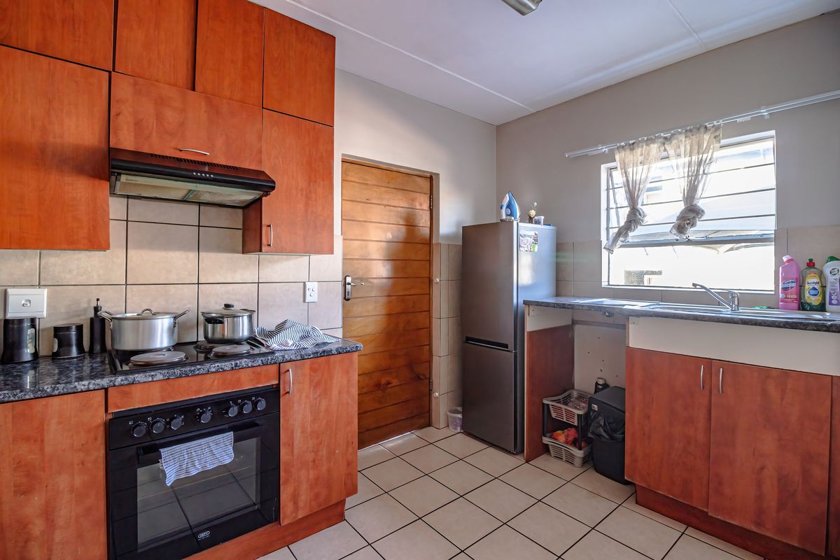 A functional kitchen featuring wooden cabinetry, built-in oven with hob, tiled backsplash, and tiled flooring, offering a practical layout for daily meal preparation.