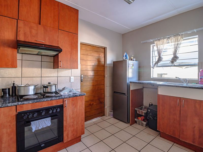 A functional kitchen featuring wooden cabinetry, built-in oven with hob, tiled backsplash, and tiled flooring, offering a practical layout for daily meal preparation.