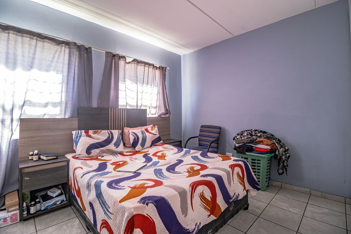 A bedroom featuring tiled flooring and a built-in headboard, providing a functional space with natural light from the windows.