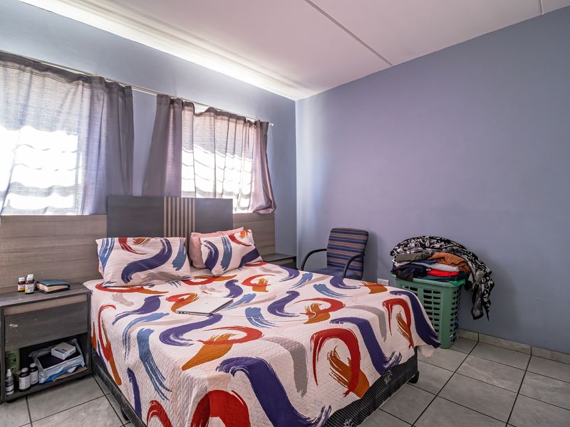 A bedroom featuring tiled flooring and a built-in headboard, providing a functional space with natural light from the windows.