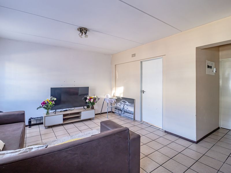 A living room featuring tiled flooring, neutral wall finishes, and an internal door leading to adjacent rooms.