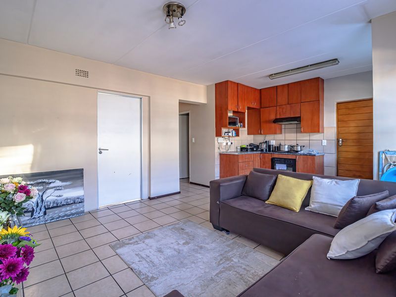 Open-plan living area featuring tiled flooring and a functional kitchen with built-in wooden cabinetry, oven, and extractor fan.