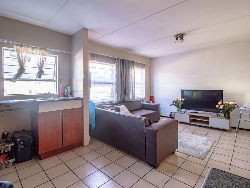 Open-plan living area featuring tiled flooring and a compact kitchen corner with built-in cabinetry and sink.