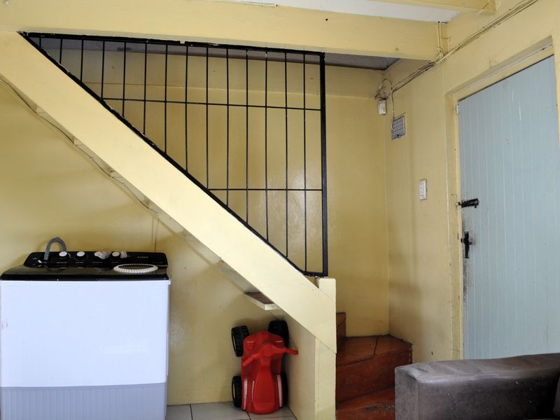 A utility area located beneath a staircase, featuring tiled flooring, a metal balustrade, and access to an internal door.