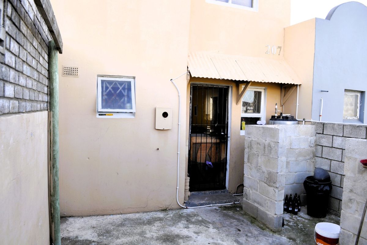 Rear exterior view of the property featuring a security gate, corrugated metal awning, and concrete block walling with an external geyser unit.