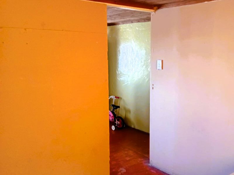 A simple interior hallway featuring timber ceiling panels, painted walls, and hardwood flooring, connecting two distinct living areas.