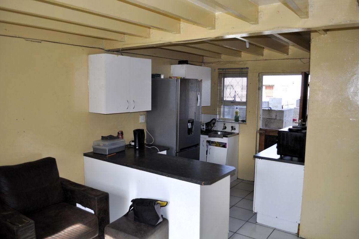 A functional kitchen featuring white cabinetry, dark countertops, and exposed ceiling beams, offering a practical layout with direct access to the exterior.