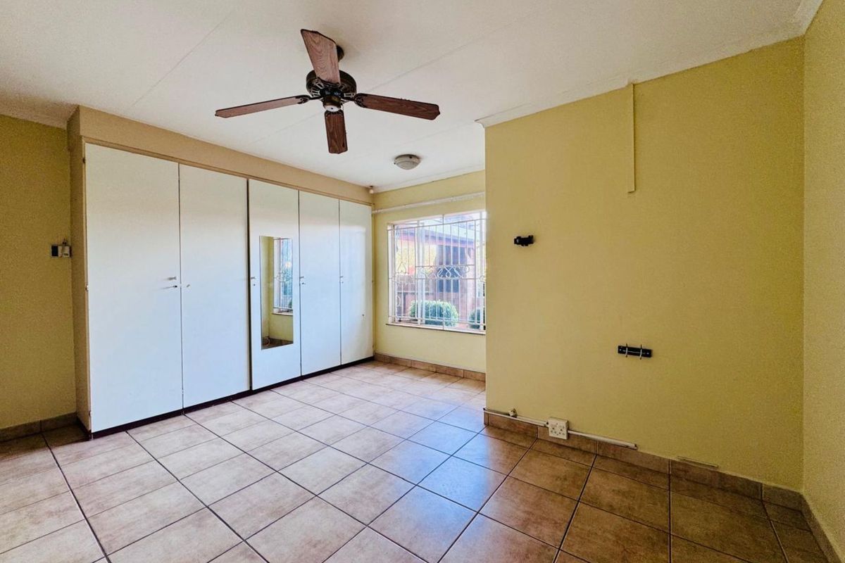 A bedroom featuring built-in cupboards, tiled flooring, a ceiling fan, and security bars on the window.