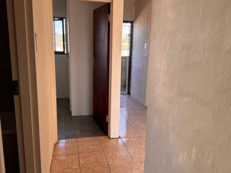 A view through a hallway featuring ceramic tiled flooring and access to adjacent rooms with timber doors and security gates.