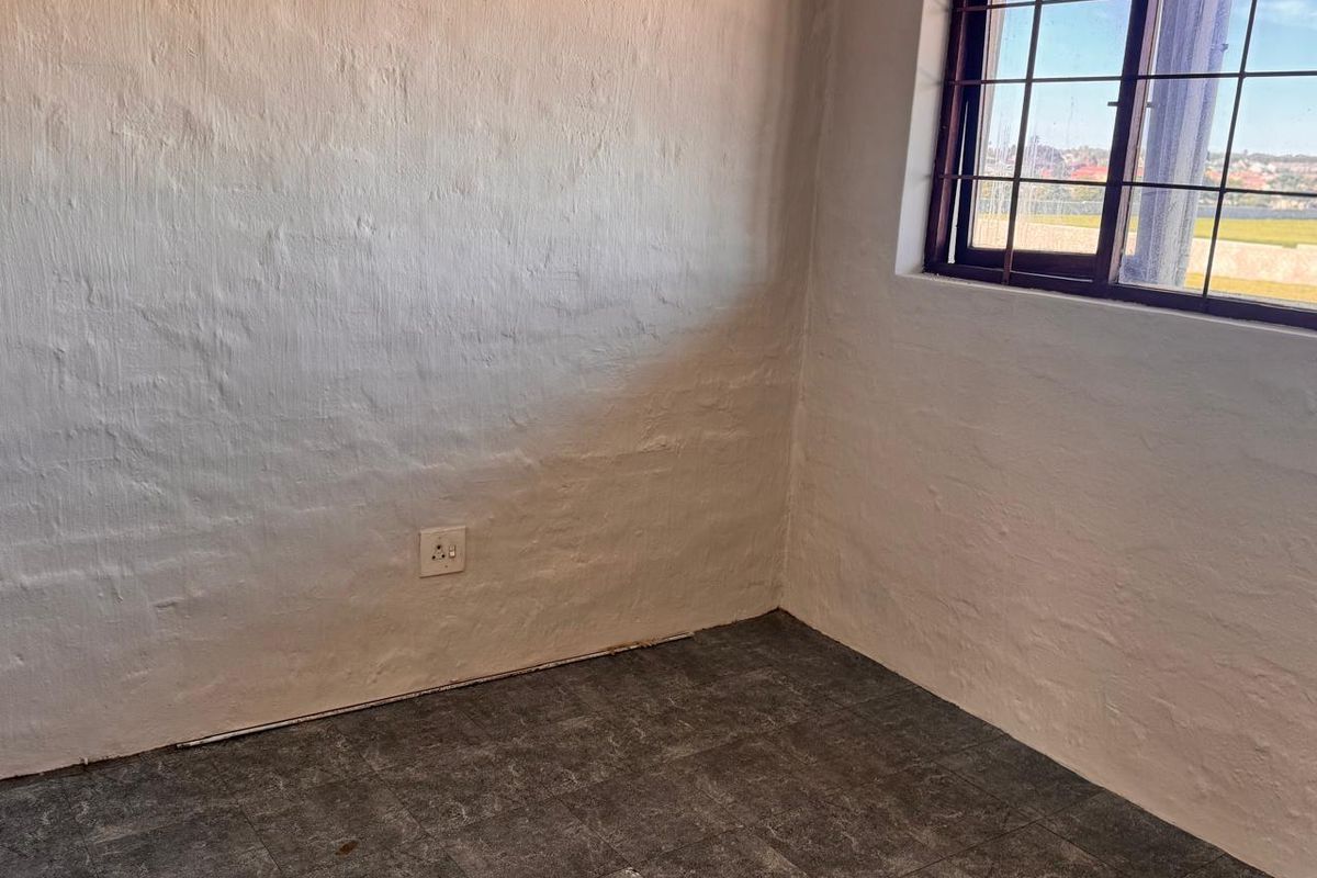 An empty bedroom featuring tiled flooring, textured walls, and a window fitted with security bars.