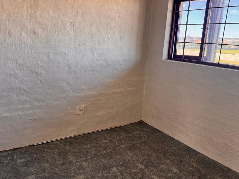 An empty bedroom featuring tiled flooring, textured walls, and a window fitted with security bars.