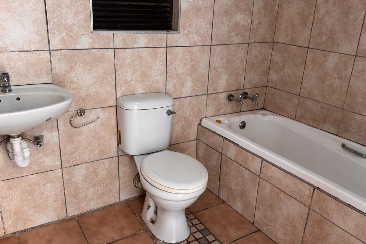 A dated bathroom featuring a standard bathtub, toilet, and wall-mounted basin with full-height wall tiling and floor tiles.