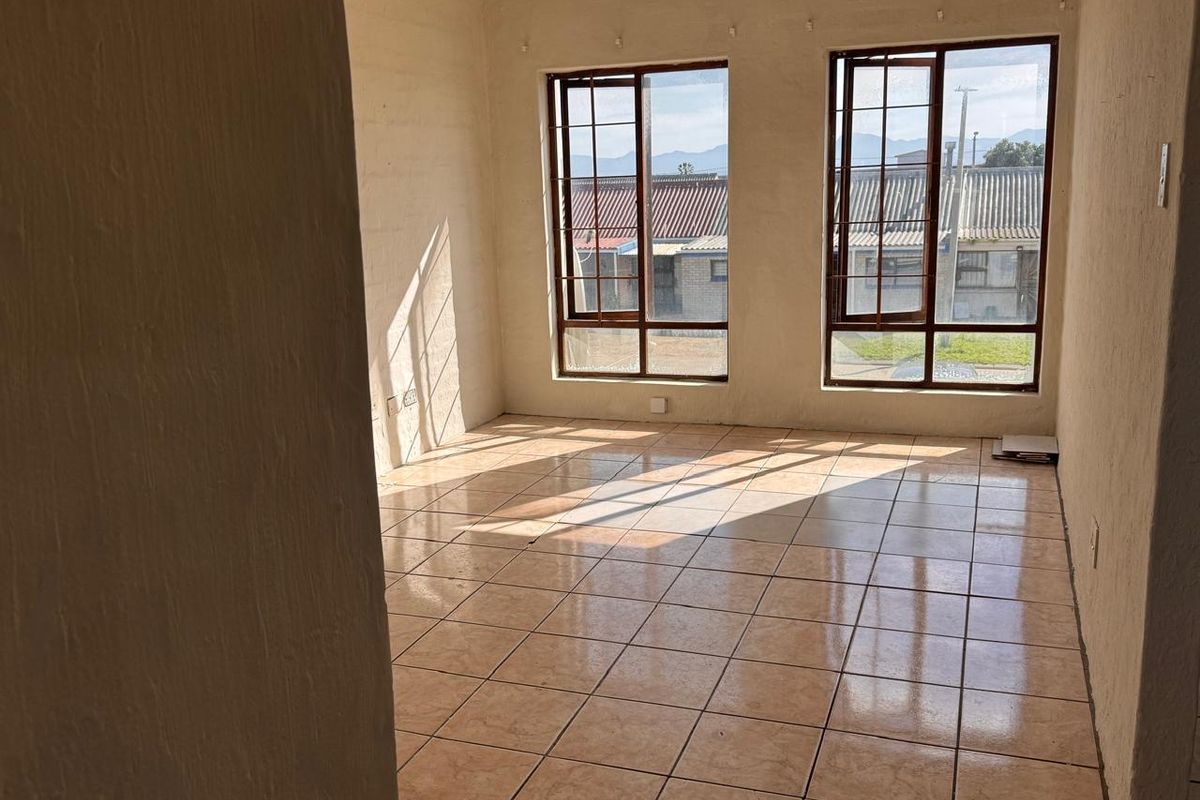 A bright, empty living area featuring tiled flooring and large windows that provide natural light and views of the surrounding neighborhood.