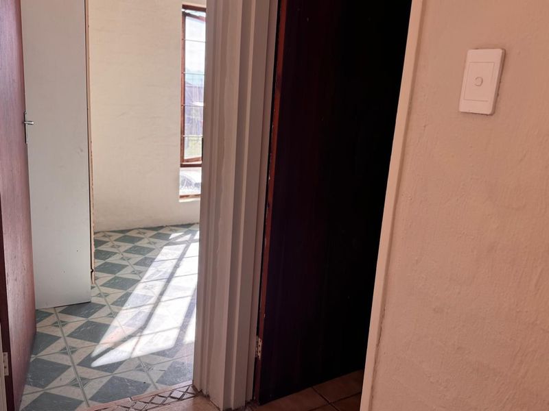 A view through a doorway into an empty hallway featuring patterned floor tiles and a timber door frame.