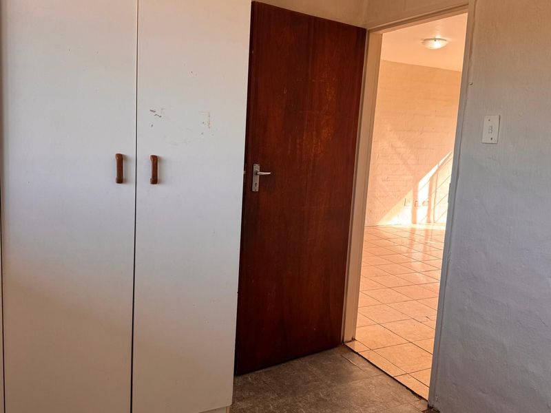 A bedroom featuring built-in wardrobes and tiled flooring, with a view into an adjacent living area.