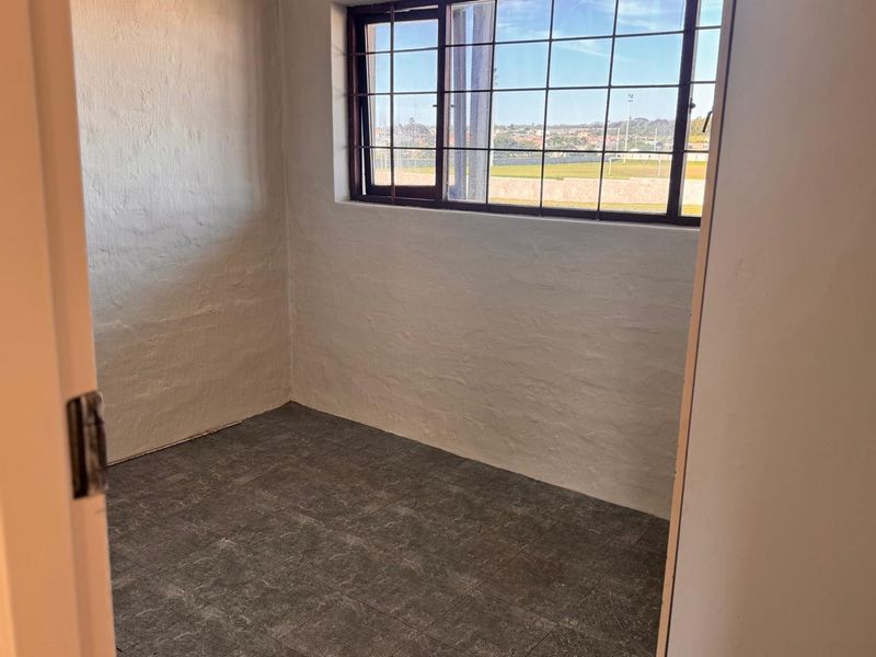 An empty bedroom featuring tiled flooring, textured walls, and a window with security bars, offering a blank canvas for potential renovation.