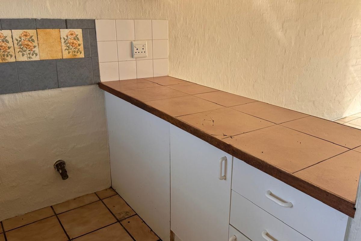 A dated kitchen area featuring tiled countertops, built-in white cabinetry, and a decorative tiled backsplash, requiring cosmetic updates.