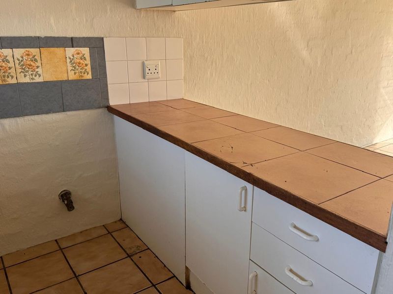 A dated kitchen area featuring tiled countertops, built-in white cabinetry, and a decorative tiled backsplash, requiring cosmetic updates.