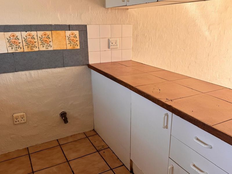 A dated kitchen area featuring tiled countertops, built-in cabinetry, and a decorative tiled splashback, currently in need of cosmetic updates.