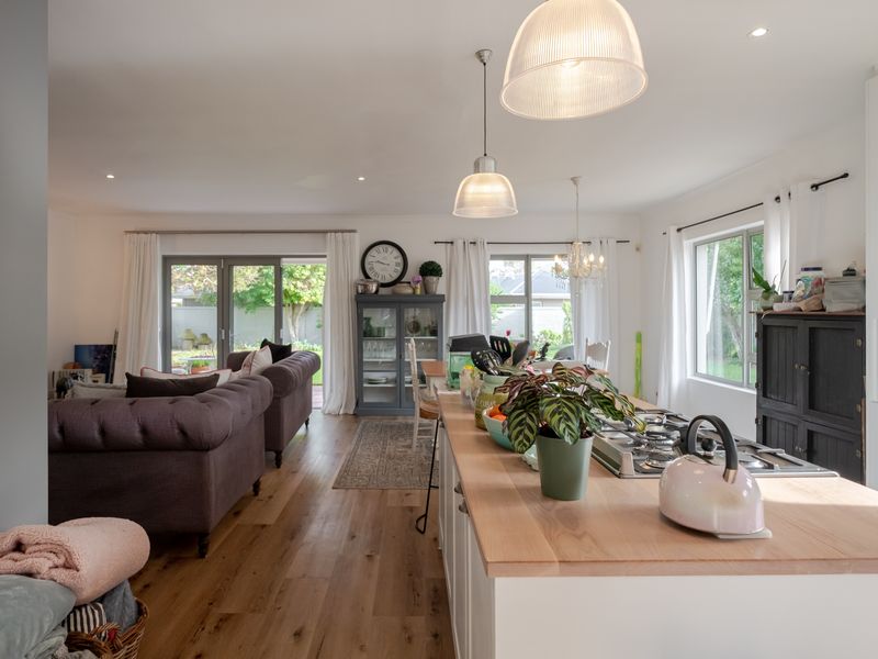 Spacious open-plan living area featuring a modern kitchen island with gas cooktop, hardwood flooring, and seamless access to the rear garden through sliding doors.