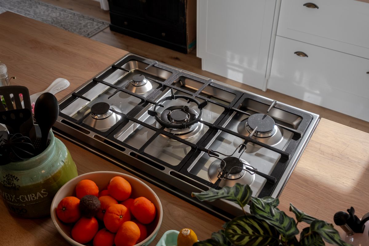 A close-up view of a modern stainless steel gas cooktop integrated into a wooden kitchen island countertop with white cabinetry.