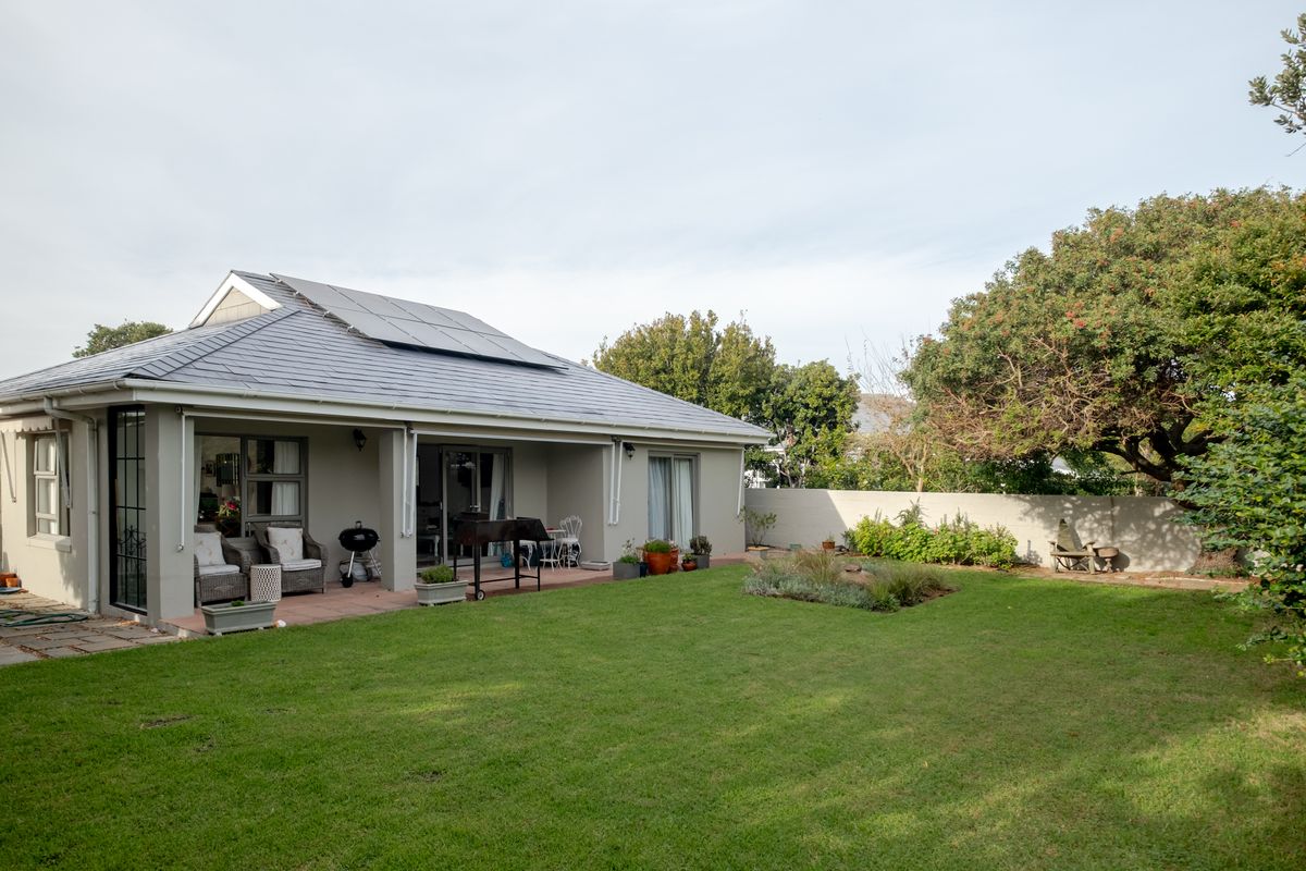 Rear view of the property featuring a covered patio, well-maintained lawn, boundary wall, and roof-mounted solar panels.