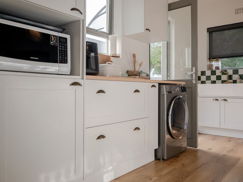 A modern, well-appointed laundry room featuring white cabinetry, timber countertops, a classic butler sink with brass tapware, and durable laminate flooring.