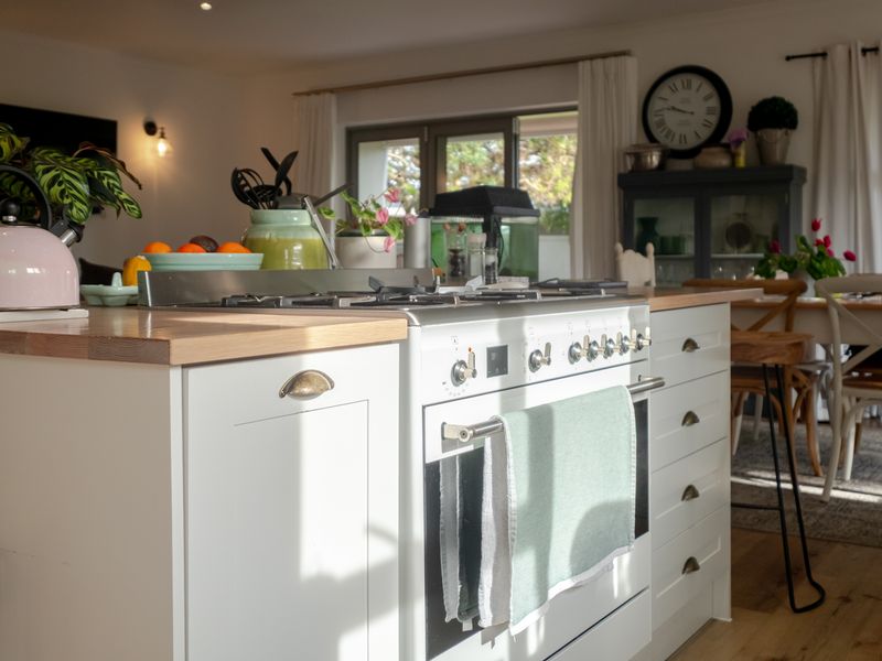 A bright open-plan kitchen featuring a central island with a gas stove, wooden countertops, and classic shaker-style cabinetry.