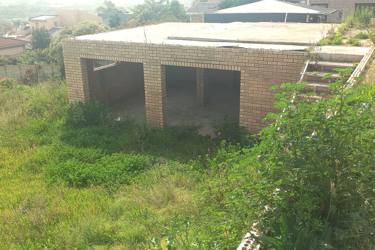 An unfinished brick garage structure situated on a sloped residential plot, featuring a concrete roof slab and external access stairs.