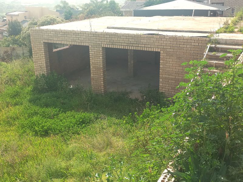 An unfinished brick garage structure situated on a sloped residential plot, featuring a concrete roof slab and external access stairs.